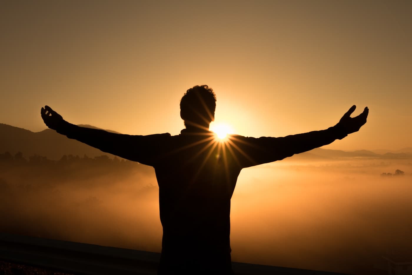 Silhouette reaching toward a sunrise over morning mist